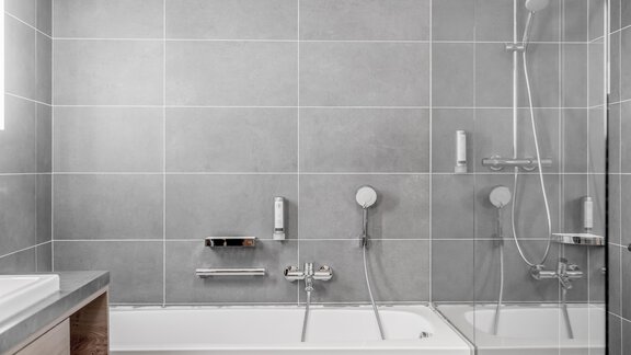 A modern bathroom with a bathtub and a rain shower. The walls are adorned with an elegant gray tile pattern. - Enzian Apartments - Hochsölden