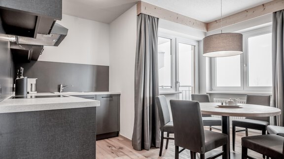 A modern kitchen with a round dining table and four chairs. Large windows let in plenty of light and create a bright atmosphere. - Enzian Apartments - Hochsölden