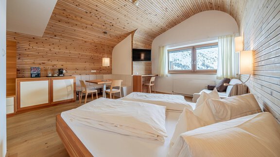 A modern bedroom with wood paneling and large windows. Two single beds and a small table with chairs are also visible. - Hotel Hochsölden - Hochsölden