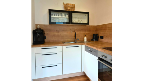 A modern kitchen with white cabinets and a wooden countertop. It is well equipped with a sink, a stove, and a coffee machine. - Apart Alessandro - Huben