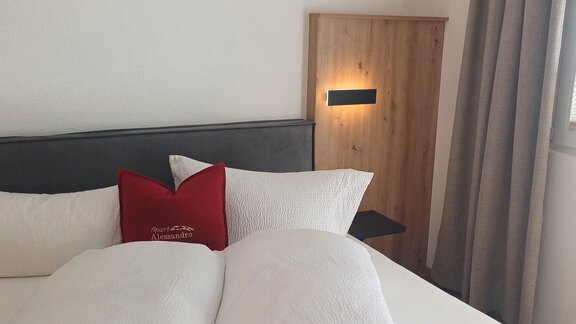 A cozy bedroom with a modern bed and soft pillows. The room is bright and inviting, with a wooden wardrobe and curtains. - Apart Alessandro - Huben