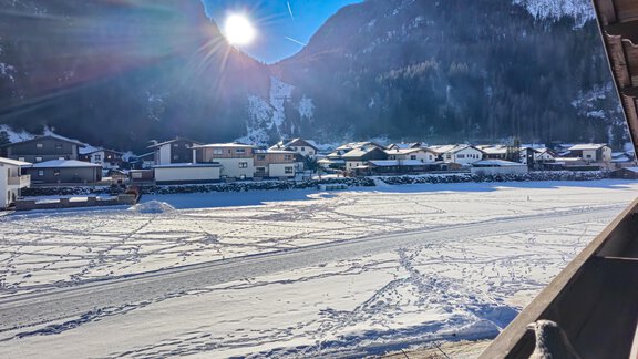 A snowy landscape with houses in the background and the sun shining in the sky. The footprints in the snow show the path through the winter landscape. - Appartements Alpenrose - Huben