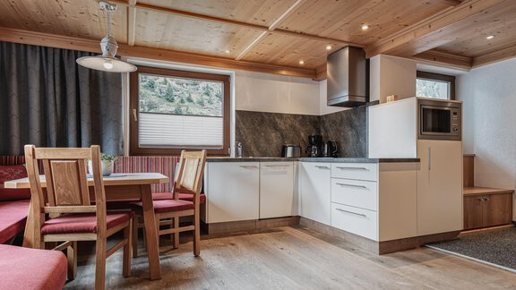 A modern kitchen with a cozy dining area and large windows. The room is bright and inviting with a wood-paneled ceiling and modern appliances. - Appartements Alpenrose - Huben