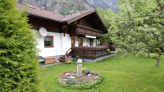 A cozy house surrounded by green grass and trees. The mountains in the background add a picturesque touch to the scene. - Appartements Gufler - Huben