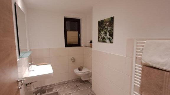 A modern bathroom with bright tiles and a washstand. A towel heater and a large window create an inviting atmosphere. - Berghaus Praxmarer - Huben