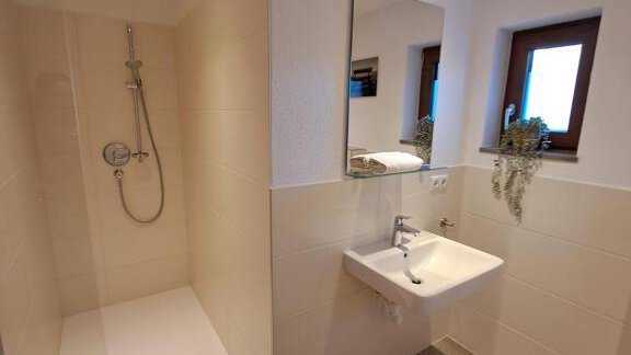 A modern bathroom with a walk-in shower and a sink. Bright tiles and a window provide plenty of light. - Berghaus Praxmarer - Huben