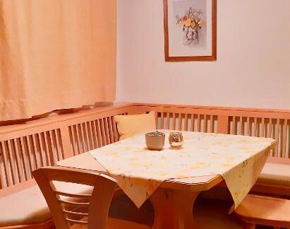 A cozy dining area with a wooden table and benches. The walls are adorned with orange curtains and there is a picture hanging on the wall. - Berghaus Praxmarer - Huben
