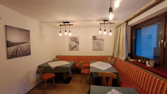 A cozy restaurant with wooden floors and orange upholstered benches. Pictures of snowy landscapes hang on the walls. - Berghaus Praxmarer - Huben