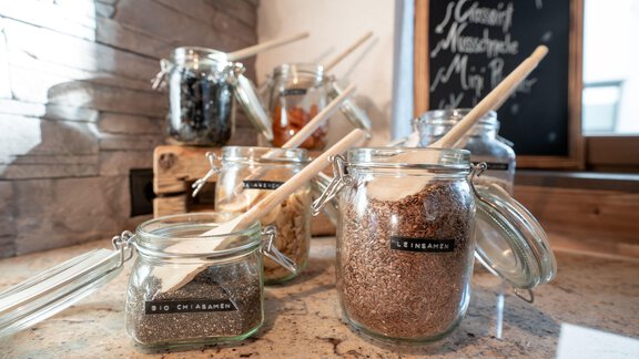 A collection of spices in jars is on a kitchen countertop. Each jar has a wooden spoon and a label. - Genusshotel Alpenblick - Huben
