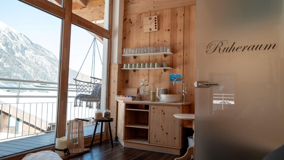A cozy relaxation room with wooden paneling and large windows. Through the windows, one looks out at the mountains and the terrace. - Genusshotel Alpenblick - Huben