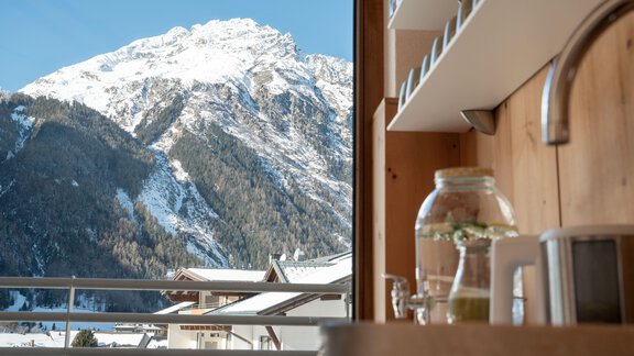 A view from a modern room of snow-covered mountains. In the foreground, elements of a kitchen can be seen. - Genusshotel Alpenblick - Huben