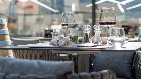 A beautifully set table in a restaurant with wine glasses and various spice containers. The surroundings are bright and modern. - Genusshotel Alpenblick - Huben