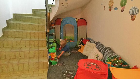 Ein Spielbereich im Untergeschoss mit bunten Spielzeugen und einem kleinen Zelt. Im Hintergrund sind Treppen und freundliche Wanddekorationen zu sehen. - Haus Max - Huben