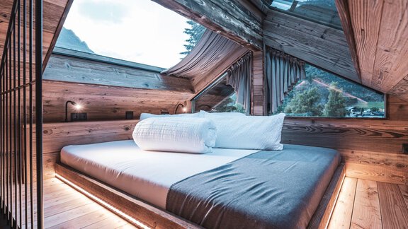 Ein modernes Schlafzimmer mit Holzdecke und großen Fenstern. Das Bett ist gemütlich und einladend, umgeben von natürlichem Licht. - Naturcamping Kuprian - Ötztal - Huben