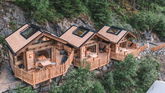 Drei Holzhäuschen stehen in der Natur, umgeben von Bäumen. Jedes Haus hat eine Veranda mit Ausblick auf die Umgebung. - Naturcamping Kuprian - Ötztal - Huben