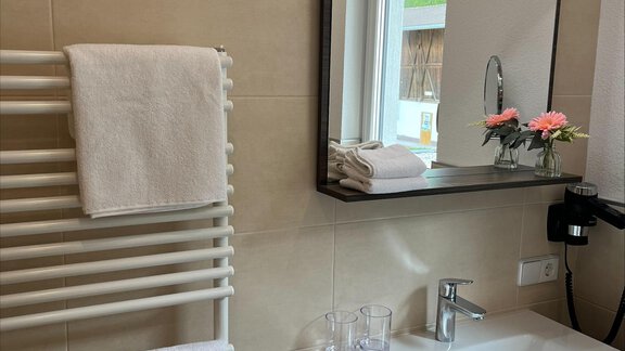 Ein modernes Badezimmer mit einem Waschbecken und einem Spiegel. Saubere Handtücher hängen an einem Handtuchhalter neben einer Fensterbank mit Blumen. - ONO Apartments - Huben