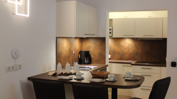 A modern kitchen corner with a small dining table and two chairs. The walls are bright, and the kitchen unit is well-equipped. - Apart Conny - Längenfeld