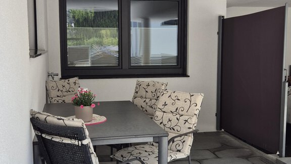 Ein gemütlicher Balkon mit einem Tisch und Stühlen. Blühende Pflanzen und ein klarer Ausblick durch die Fenster sorgen für eine entspannte Atmosphäre. - Apart Fiegl Längenfeld - Längenfeld