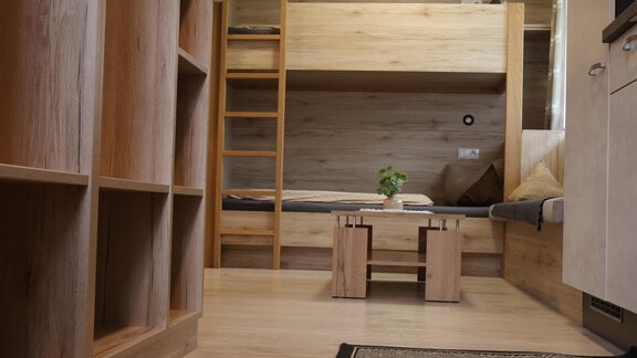 A cozy room with a bunk bed and a small table. The floor is made of wood and the room has some shelves. - Apart Katja - Längenfeld