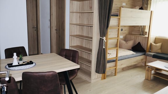 A modernly furnished room with a dining table and a bunk bed. The walls have a wood look, and there is a cozy sitting area. - Apart Katja - Längenfeld