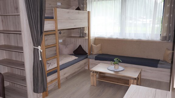 A modern room with a loft bed and a cozy seating area. The bright wooden paneling and windows create a friendly atmosphere. - Apart Katja - Längenfeld