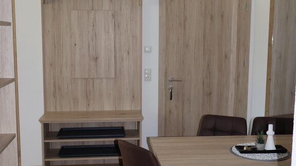 A bright room with a wooden table and chairs.  
On the wall, there is a cabinet and a door leads outside. - Apart Katja - Längenfeld