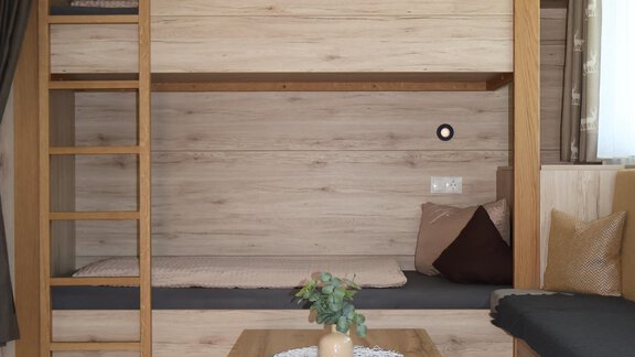 A modern bedroom with a wooden bunk bed and a cozy seating area. The room has a warm, inviting atmosphere and is well-lit. - Apart Katja - Längenfeld