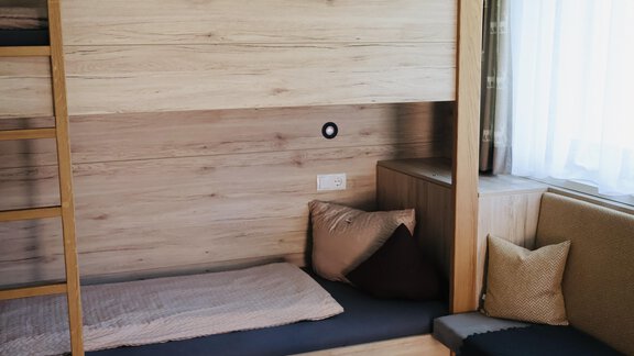 The image shows a cozy room with a wooden bunk bed and a seating area. Large windows let in plenty of light and create an inviting atmosphere. - Apart Katja - Längenfeld