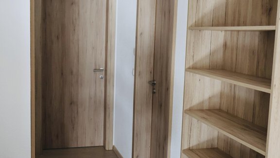 A bright room with wooden doors and an open shelf. The floor is made of wood and the walls are kept neutral. - Apart Katja - Längenfeld