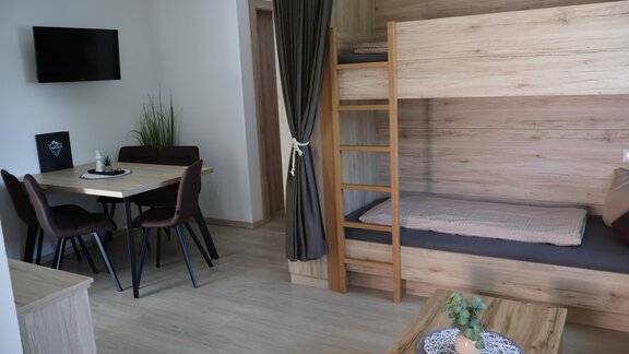 A modern room with wooden furnishings. It includes a bunk bed, a dining area, and a wall-mounted television. - Apart Katja - Längenfeld