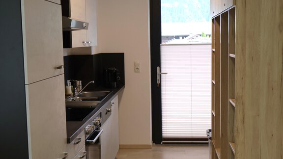 A modern kitchen with light cabinets and a black countertop. It has a large window front that lets in a lot of light. - Apart Katja - Längenfeld