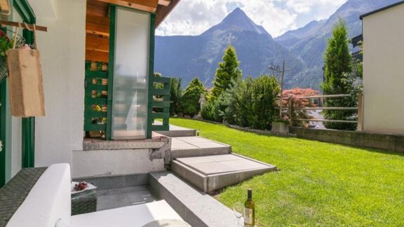 Ein gemütlicher Außenbereich mit einer Sitzgelegenheit und Blick auf die Berge. Der Rasen ist grün und gepflegt, ideal zum Entspannen. - Apartment DoLa - Längenfeld