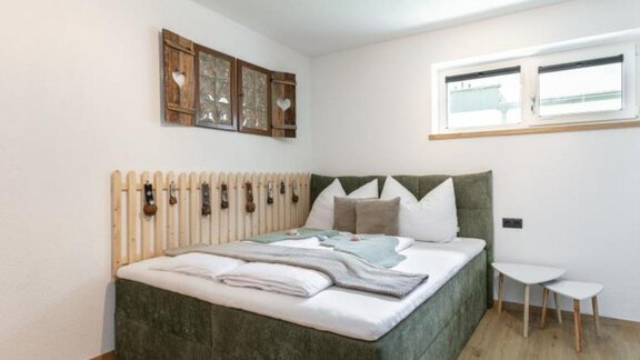 Ein modernes Schlafzimmer mit einem bequemen grünen Bett und künstlerischen Dekorationen an der Wand. Der Holzfußboden und die hellen Wände schaffen eine gemütliche Atmosphäre. - Apartment DoLa - Längenfeld