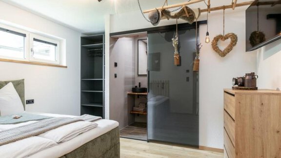 A modern bedroom with a cozy bed edge and wooden furniture. The room is bright and well-structured, featuring a dressing area and a bathroom. - Apartment DoLa - Längenfeld
