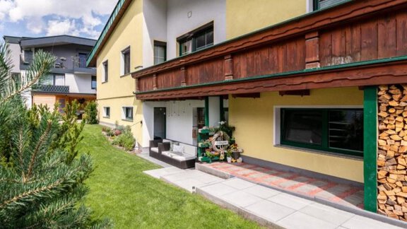 A modern house facade with a well-kept garden and wood storage. The entrance is inviting and has a cozy character. - Apartment DoLa - Längenfeld