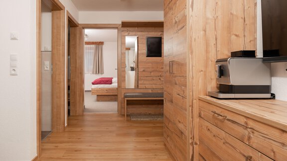Ein heller Flur mit hölzernen Möbeln und einem Fernseher. Im Hintergrund sind weitere Räume mit einem roten Bett sichtbar. - Appart Klotz Alpenglück - Längenfeld