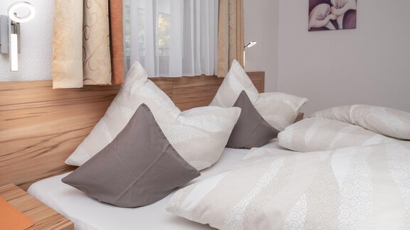 Ein gemütliches Schlafzimmer mit einem Bett, das mit weichen Kissen und Decken dekoriert ist. Im Hintergrund sind sanfte Vorhänge und ein Kunstwerk an der Wand zu sehen. - Appart Klotz Alpenglück - Längenfeld