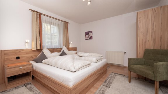 Ein modernes Schlafzimmer mit einem gemütlichen Bett und einer grünen Sitzecke. Helle Wände und Holzmöbel sorgen für eine angenehme Atmosphäre. - Appart Klotz Alpenglück - Längenfeld