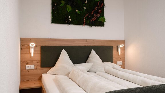 Ein gemütliches Schlafzimmer mit einem Doppelbett und einer modernen Holzverkleidung. An der Wand hängt ein dekoratives Kunstwerk aus Pflanzen. - Appart Klotz Alpenglück - Längenfeld
