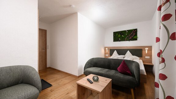 Ein gemütliches Zimmer mit Holzfußboden und modernem Mobiliar. Die Einrichtung umfasst ein Sofa, einen Tisch und ein Doppelbett mit Kissen. - Appart Klotz Alpenglück - Längenfeld