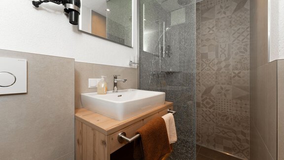 Ein modernes Badezimmer mit einer Dusche und einem eleganten Waschbecken aus Holz. Die Wände sind hell gefliest und der Raum strahlt eine schlichte Eleganz aus. - Appart Klotz Alpenglück - Längenfeld