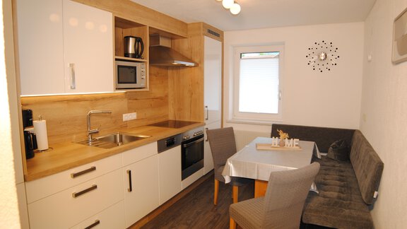 A modern kitchen with bright wood details and white cabinets. At the table are three chairs and a cozy seating area. - Appart Tanja - Längenfeld