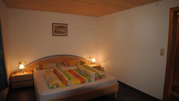 A simple bedroom with a large bed and colorful pillows. The walls are brightly painted and there is soft lighting. - Appart Tanja - Längenfeld
