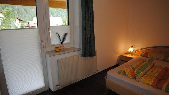 A cozy bedroom with a bed and colorful bed sheets. The window offers a view of greenery and lets in plenty of daylight. - Appart Tanja - Längenfeld