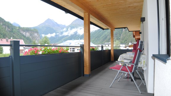 A balcony with wooden cladding and a view of the mountains. Two sun loungers are placed on the balcony, surrounded by flowers. - Appart Tanja - Längenfeld
