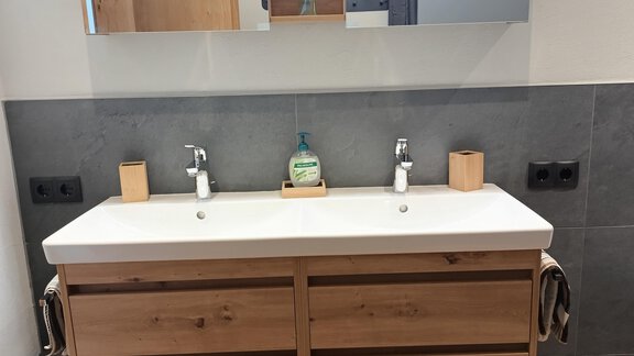 A modern bathroom with a wooden washbasin and two sinks. In the background, a mirror and some decorative details can be seen. - Appartement Thermenzeit - Längenfeld