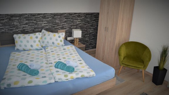 A modern bedroom with a large bed and colorful bedding. Next to it is a stylish armchair and a small plant decorates the room. - Appartement Thermenzeit - Längenfeld