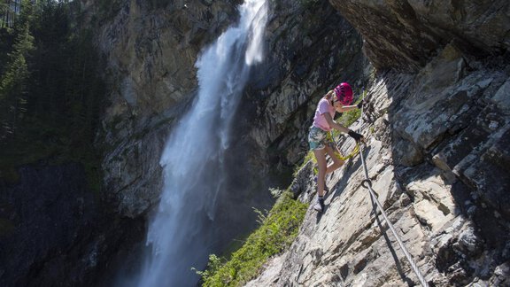 A person is climbing a rock face near a waterfall. The surroundings are characterized by trees and rocks. - Bauernhaus Auer - Längenfeld