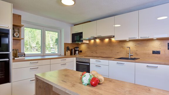 Eine moderne Küche mit Holz- und weißen Schränken. Auf der Kücheninsel liegen frisches Gemüse und Obst. - Ferienhaus Schrankogelblick - Längenfeld