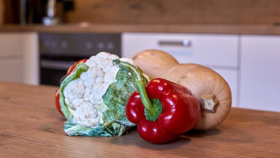 Eine Auswahl an frischem Gemüse liegt auf einem Holztisch. Darunter befinden sich Blumenkohl, eine rote Paprika und ein Butternusskürbis. - Ferienhaus Schrankogelblick - Längenfeld